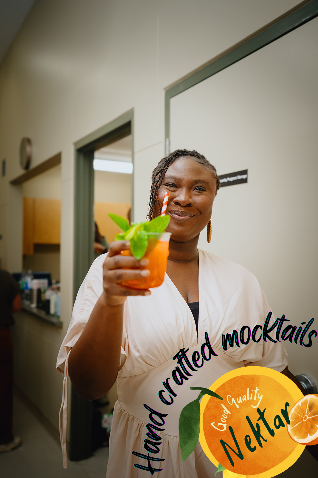 Guest holding up an orange hand-crafted Nektar mocktail garnished with mint at a Saskatoon event
